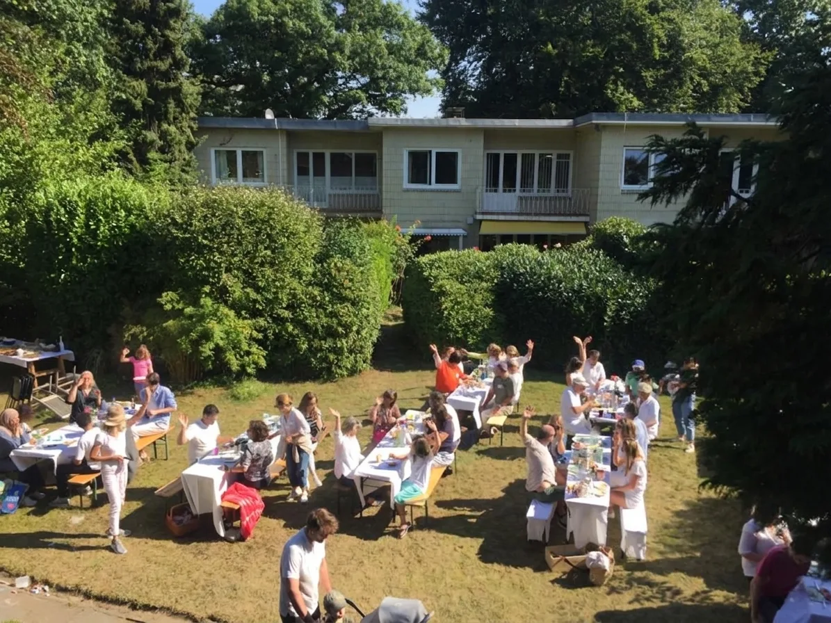 Nachbarn des Pikartenkamps beim Straßenfest 2022: lange Tafeln auf der Wiese, Familien mit Kindern essen und lachen miteinander